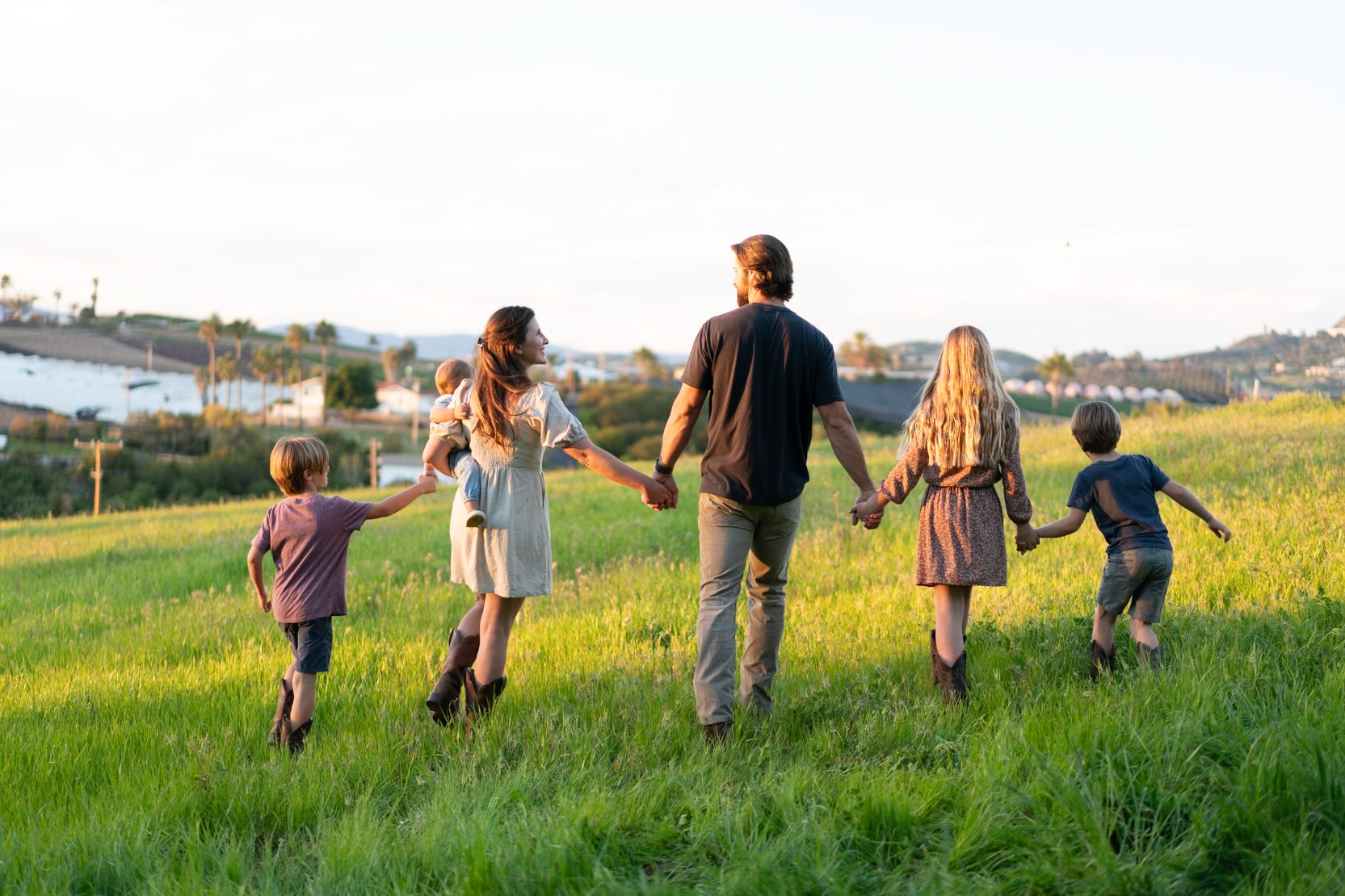 The Schleicher family walking hand in hand through a sunlit green field at golden hour.