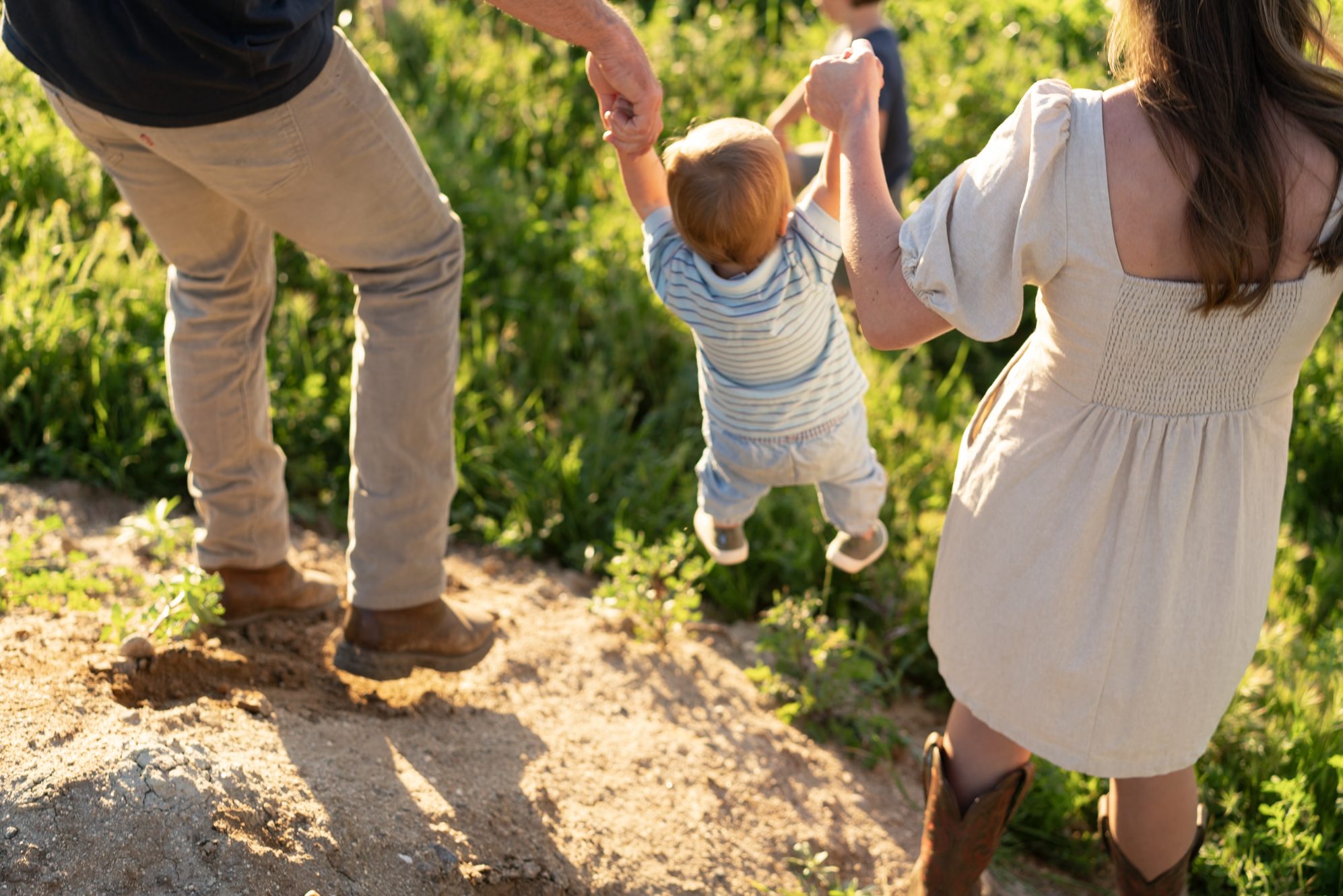 Steven and Sheena swinging their youngest between them on a sunlit trail.