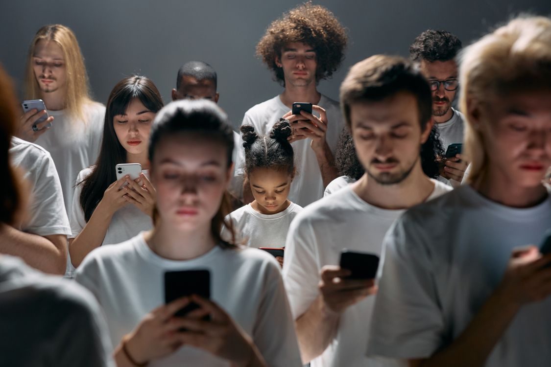 A crowd of people of many ages, heads down, each looking into their own phone.